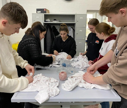 Junge Menschen stehen an einem Tisch und knoten weiße Strümpfe zusammen