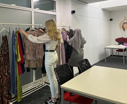 Junge Frau steht vor einem Kleiderständer mit Klamotten und sieht sich diese an.