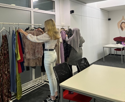 Junge Frau steht vor einem Kleiderständer mit Klamotten und sieht sich diese an.