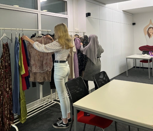 Junge Frau steht vor einem Kleiderständer mit Klamotten und sieht sich diese an.