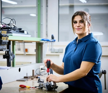 Junge Frau steht an einer Werkbank und hält einen Schraubendreher in der Hand