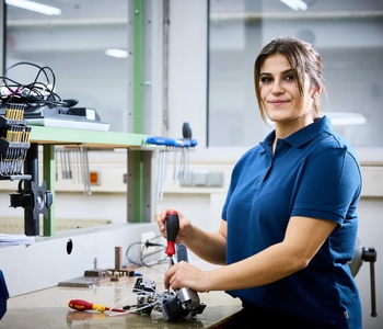 Junge Frau steht an einer Werkbank und hält einen Schraubendreher in der Hand