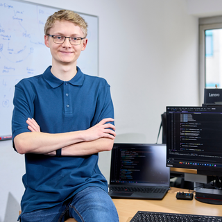 Junger Mann sitzt lässig auf seinem Schreibtisch