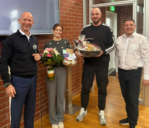 Drei Männer und eine Frau mit Blumenstrauß und Präsentkorb