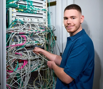 Junger Mann steht vor einem Schaltschrank mit verschiedenen Kabeln