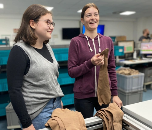 Eine Auszubildende zeigt einer Schülerin einen Strumpf