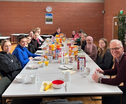 Viele Jugendliche sitzen zusammen mit ihrem Vorgesetzten an einer langen Tafel und frühstücken.