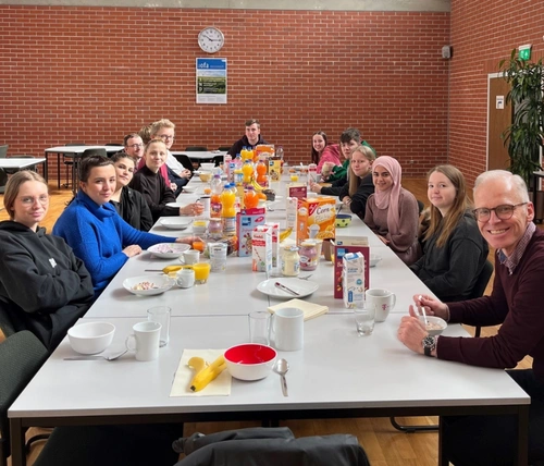 Viele Jugendliche sitzen zusammen mit ihrem Vorgesetzten an einer langen Tafel und frühstücken.