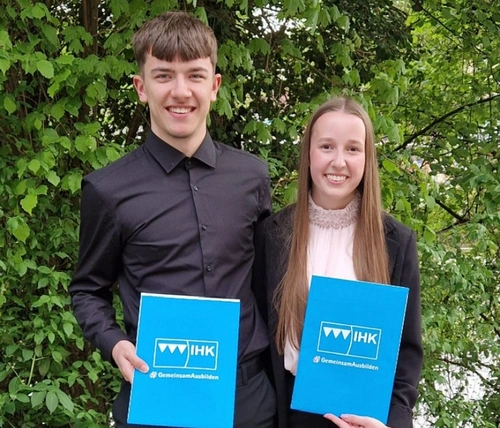 Zwei Jugendliche in festlichen Outfits halten eine Mappe in der Hand