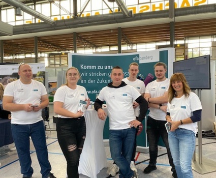 Auszubildende und Ausbilder in einheitlichen T-Shirts stehen vor einem Messestand auf der Azubimesse in Glauchau