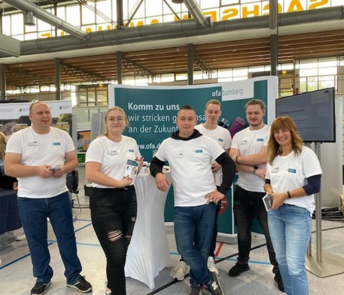 Auszubildende und Ausbilder in einheitlichen T-Shirts stehen vor einem Messestand auf der Azubimesse in Glauchau