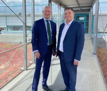 Zwei Männer im Anzug auf einem Steg, der über ein Gebäude führt